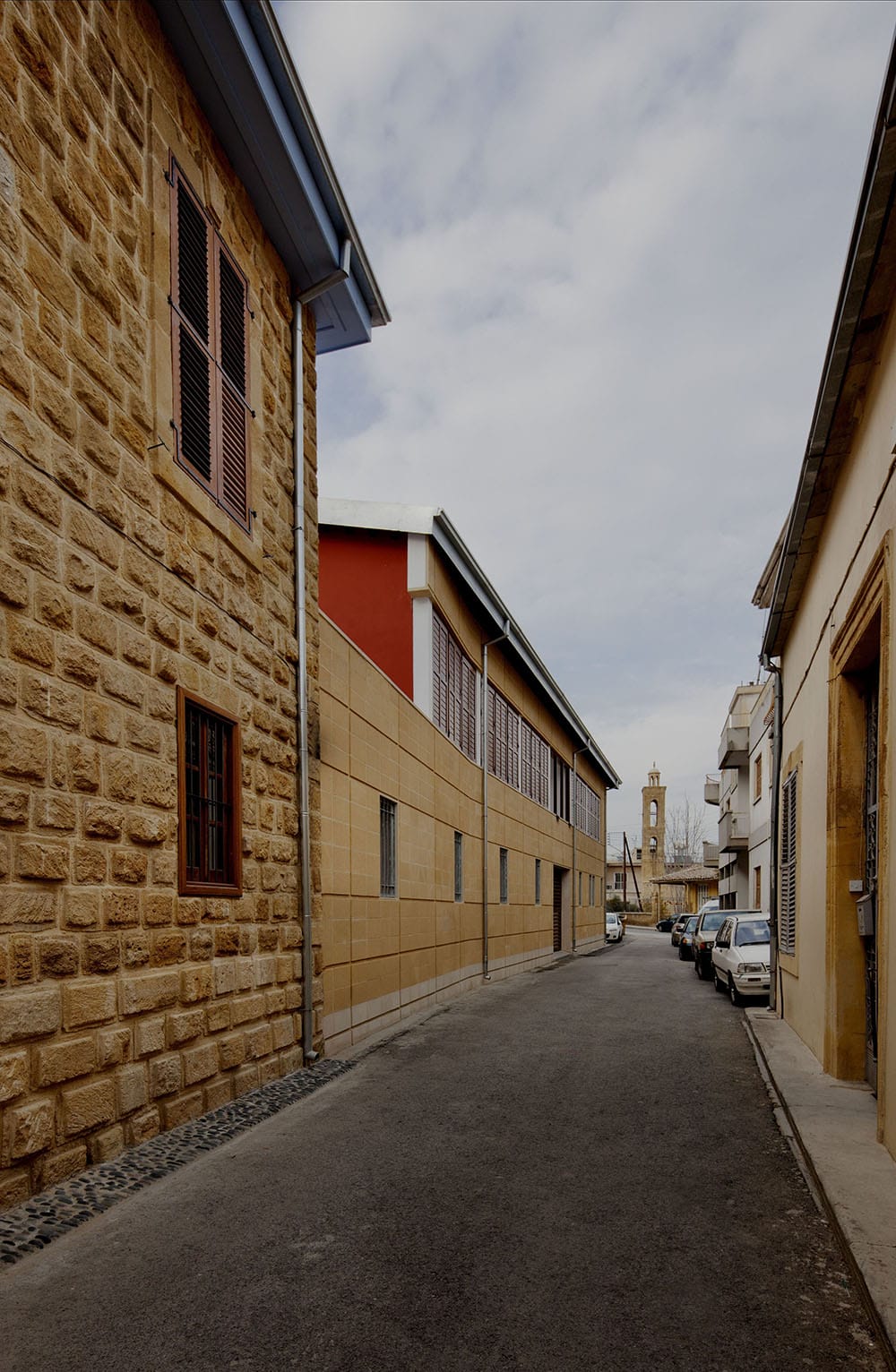 Οδός Αρχιμανδρίτη Κυπριανού από νότια προς βόρεια.  Το παλιό διατηρητέο διώροφο ανακαινίστηκε και δεξιά-αριστερά προστέθηκαν δύο νέες πτέρυγες πάνω στο ίχνος των κτιρίων που προϋπήρχαν (σύμφωνα με τα χωρομετρικά σχέδια), αποκαθιστώντας έτσι τον οικοδομικό ιστό της παλιάς πόλης.  Στο βάθος το καμπαναριό του Αγίου Αντωνίου, © Creative Photo Room
