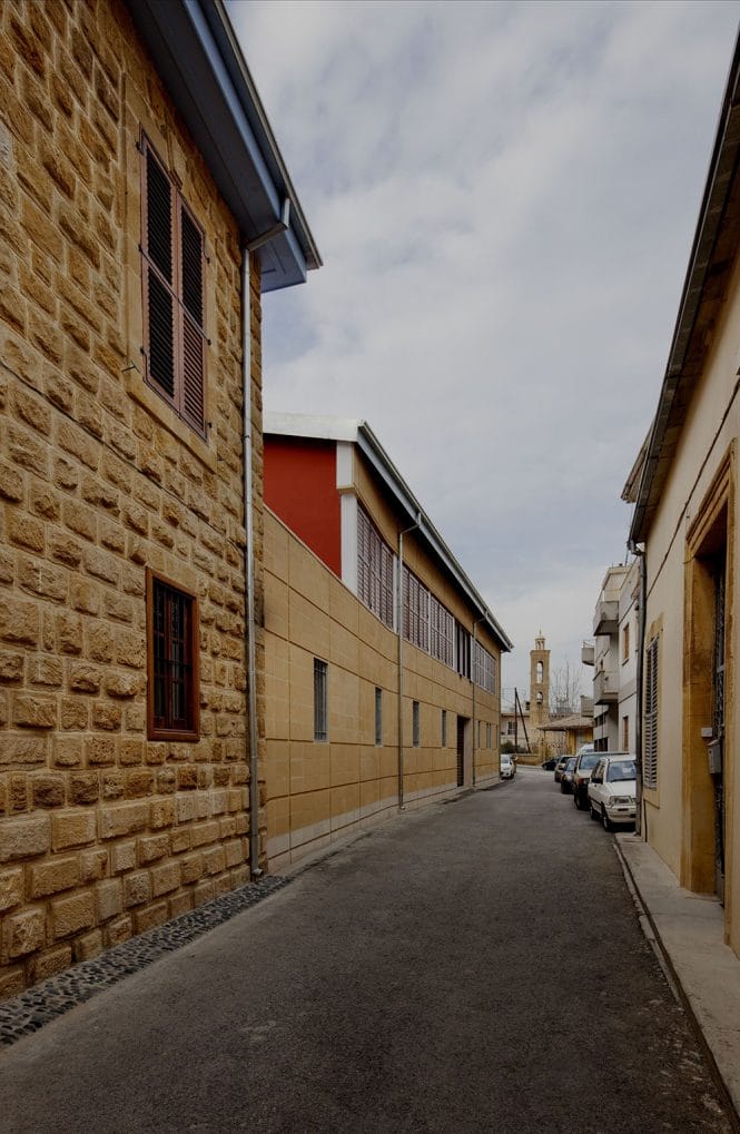 Οδός Αρχιμανδρίτη Κυπριανού από νότια προς βόρεια.  Το παλιό διατηρητέο διώροφο ανακαινίστηκε και δεξιά-αριστερά προστέθηκαν δύο νέες πτέρυγες πάνω στο ίχνος των κτιρίων που προϋπήρχαν (σύμφωνα με τα χωρομετρικά σχέδια), αποκαθιστώντας έτσι τον οικοδομικό ιστό της παλιάς πόλης.  Στο βάθος το καμπαναριό του Αγίου Αντωνίου, © Creative Photo Room