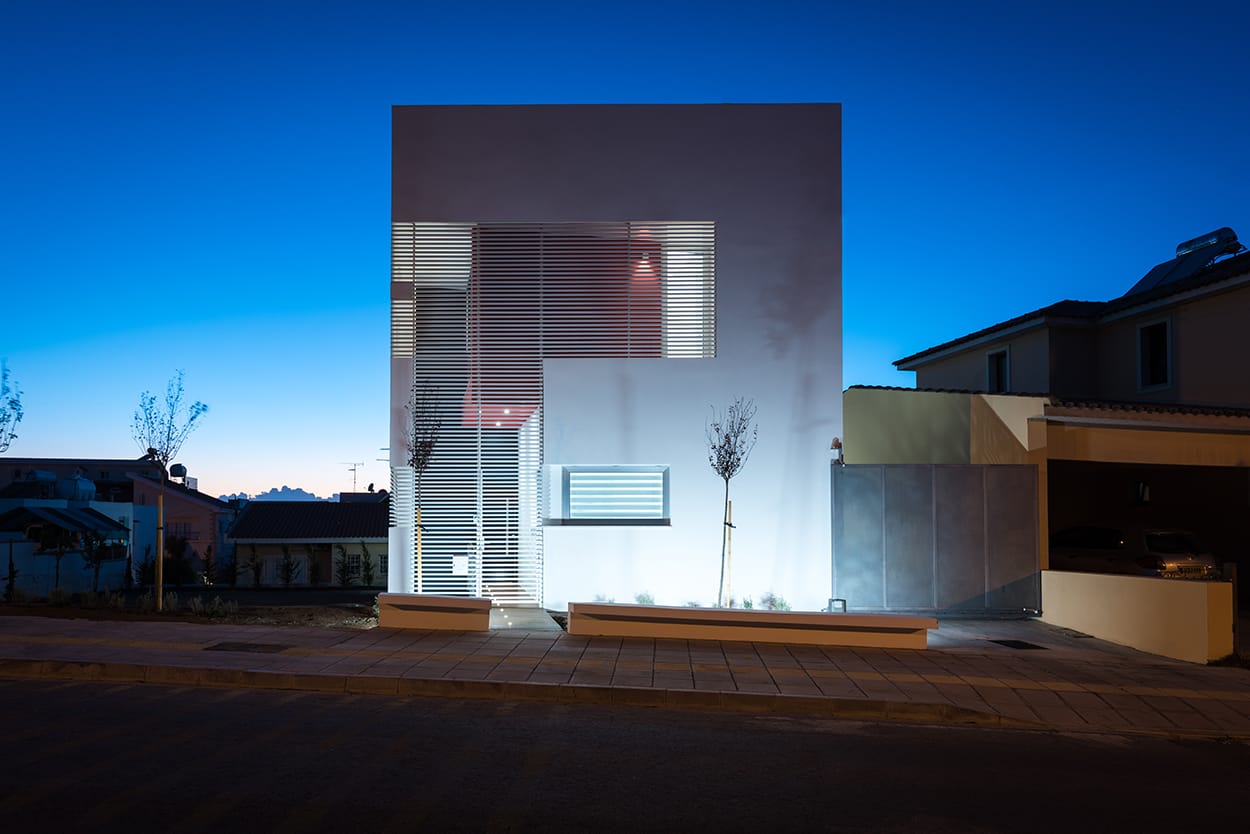 Νυχτερινή άποψη της πρόσοψης (ανατολικής όψης) της κατοικίας. Οι λεπτές δοκίδες αλουμινίου λειτουργούν ως φίλτρα, συμβάλλοντας και καθορίζοντας την αισθητική ταυτότητα του κτιρίου, © Χάρης Σολωμού (Architectural Photography)